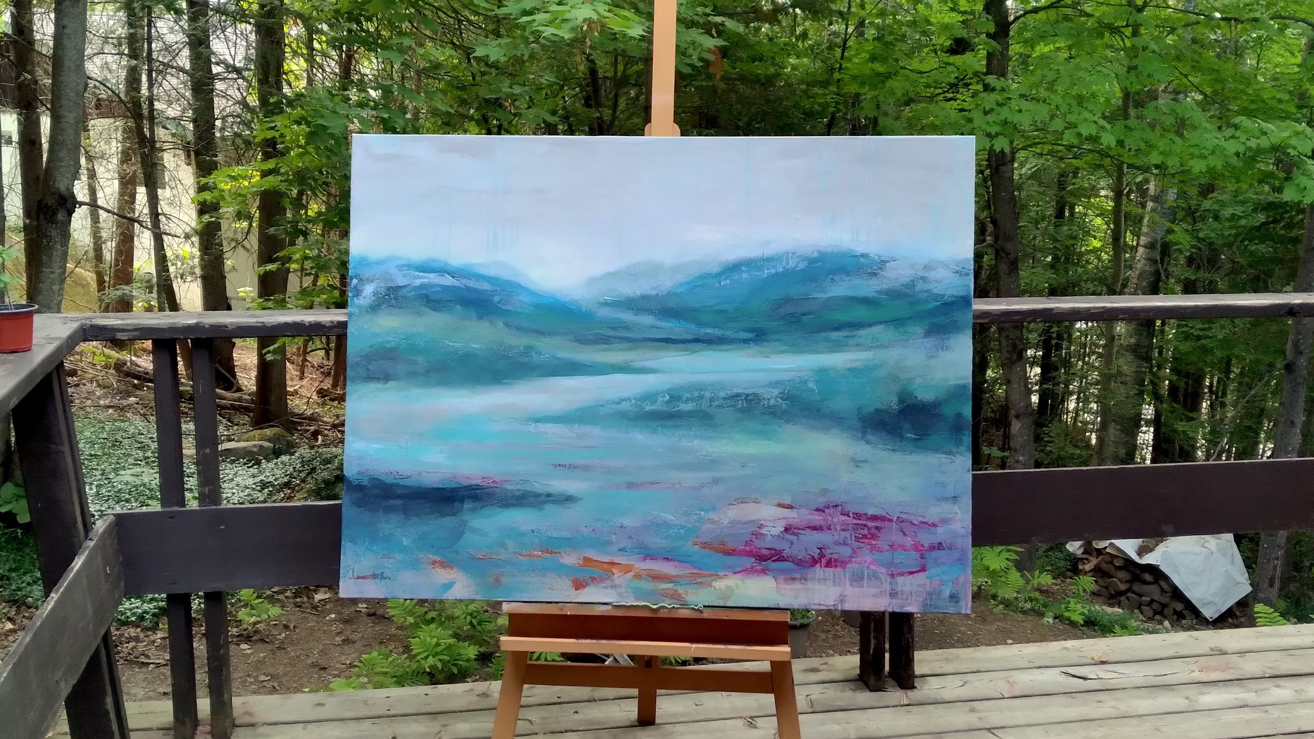 Image de la toile Au fil de l'eau, 36x48 po, présentée à l'extérieur. Peinture acrylique abstraite, suggérant un paysage avec des montagnes, un lac ou une rivière. Couleur turquoise